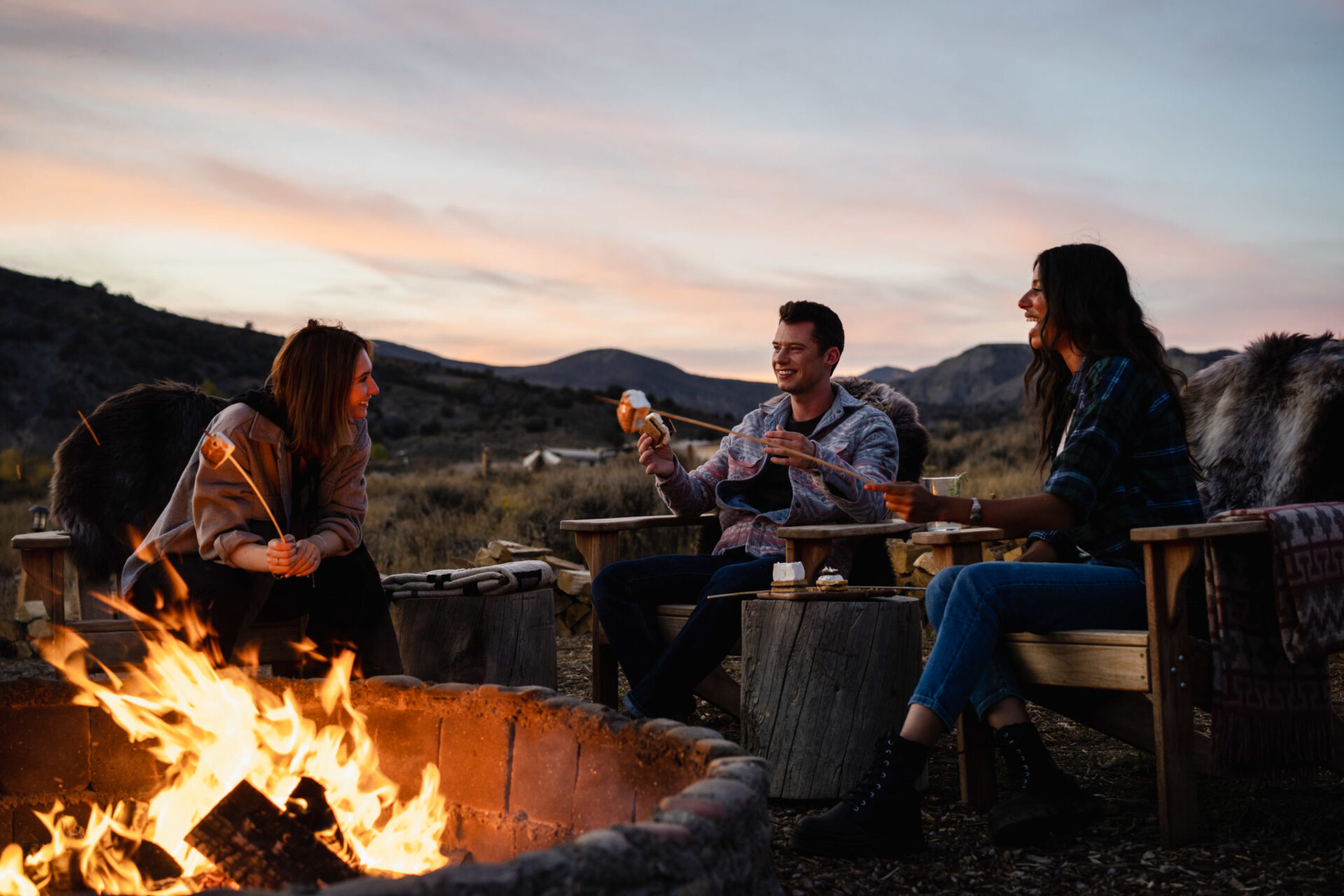 Two women and man sitting with campfire in the afternoon