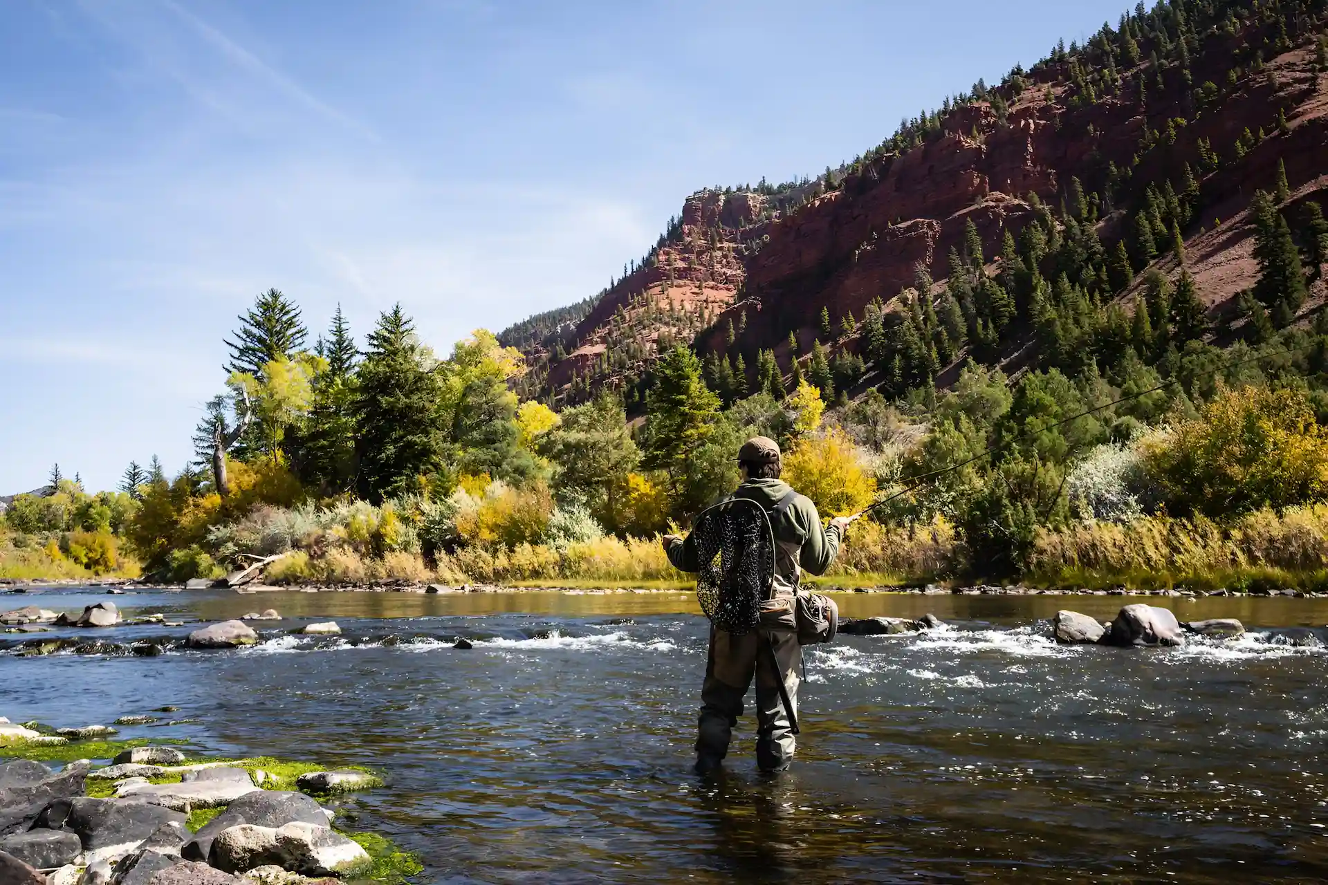 A man is fly fishing in the river at our luxury camping retreat in Vail, Colorado.